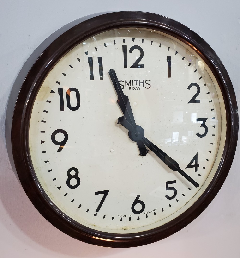 A circular wall clock with a dark brown Bakelite frame, cream dial, bold black numerals, and black clock hands. View V
