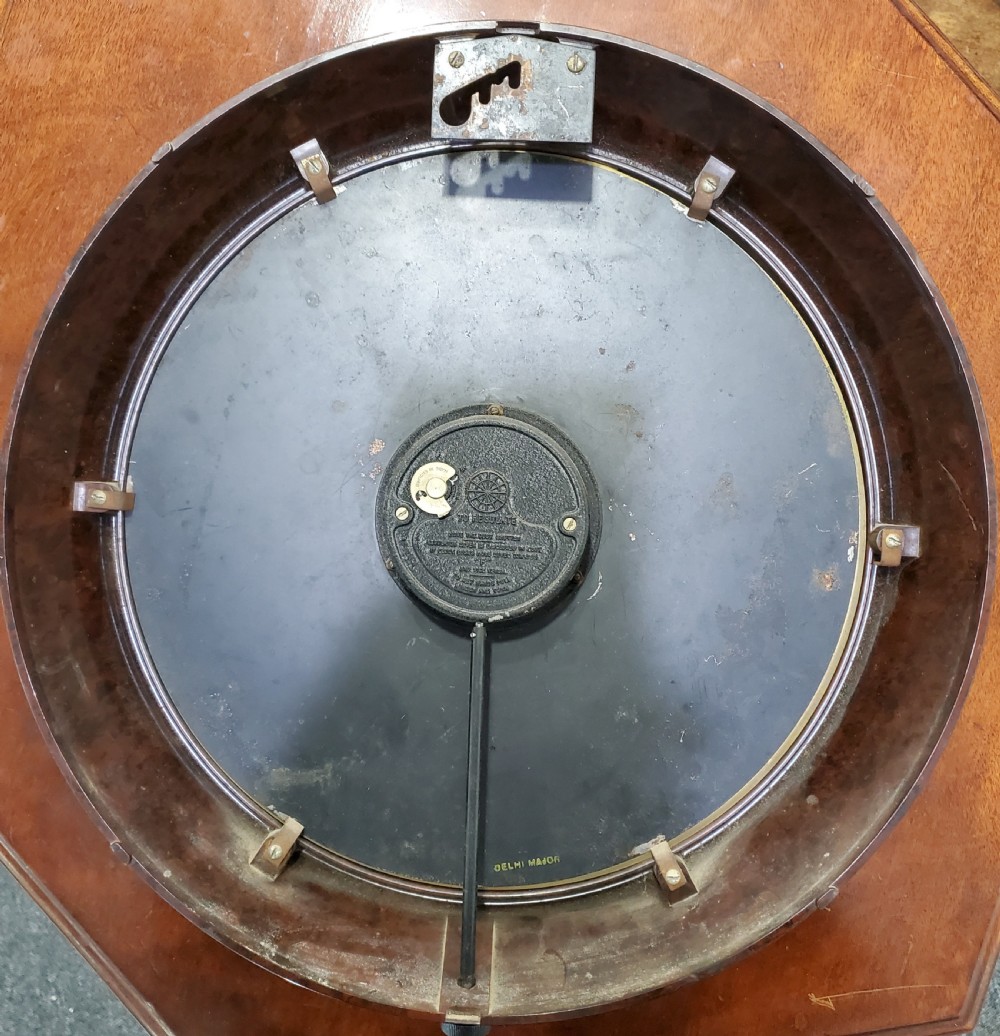 A circular wall clock with a dark brown Bakelite frame, cream dial, bold black numerals, and black clock hands. View VI