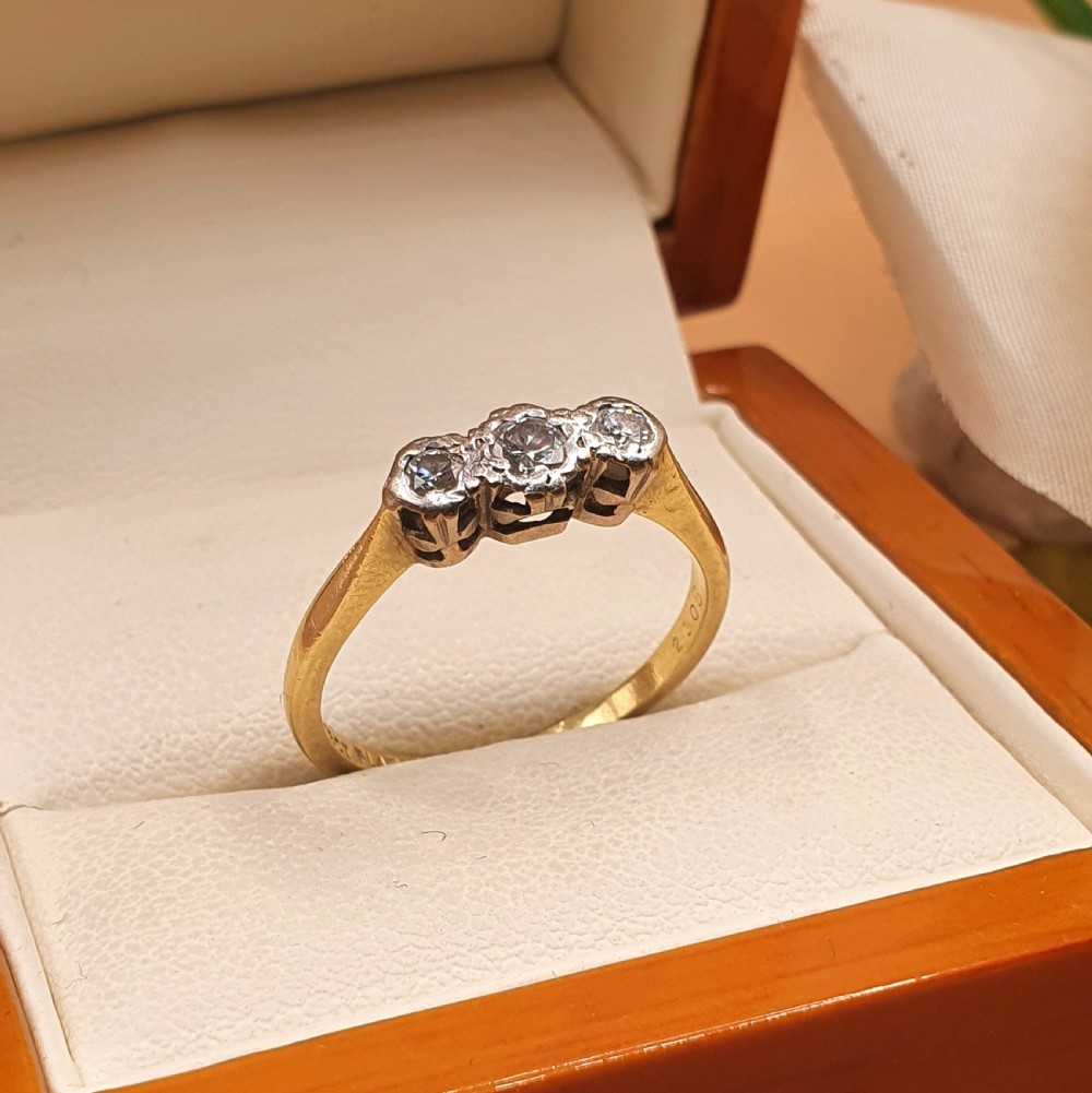An Art Deco trilogy ring featuring three round diamonds set in a platinum mount on an 18ct yellow gold band.