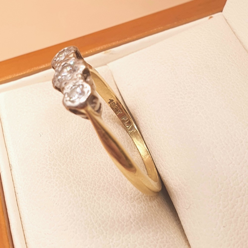 An Art Deco trilogy ring featuring three round diamonds set in a platinum mount on an 18ct yellow gold band. View IV