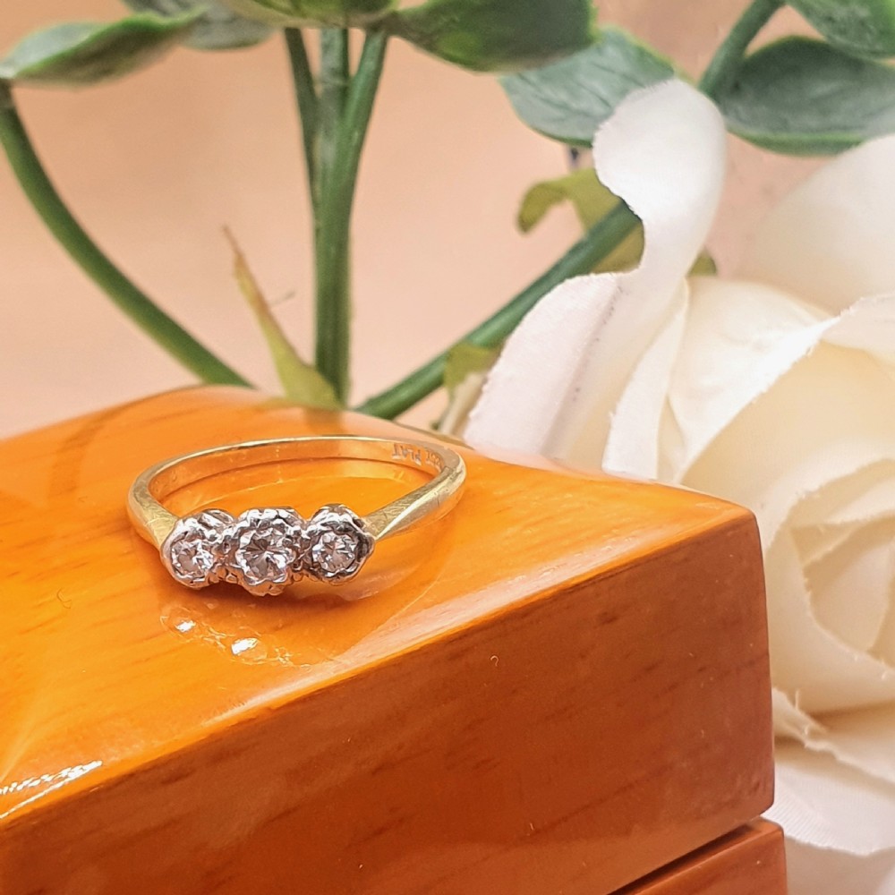 An Art Deco trilogy ring featuring three round diamonds set in a platinum mount on an 18ct yellow gold band. View V