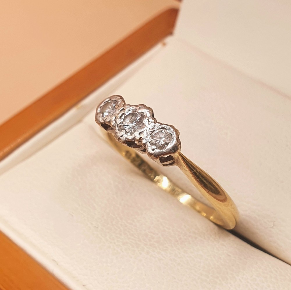 An Art Deco trilogy ring featuring three round diamonds set in a platinum mount on an 18ct yellow gold band. View VI