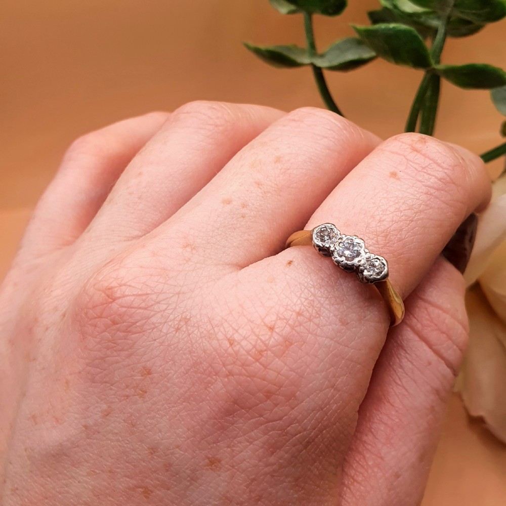 An Art Deco trilogy ring featuring three round diamonds set in a platinum mount on an 18ct yellow gold band. View IX