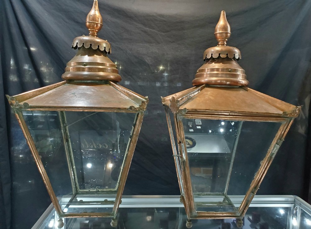 A pair of late Victorian copper lanterns featuring glazed four-sided glass bodies, tapered bases, and decorative turned finials atop scalloped hoods.