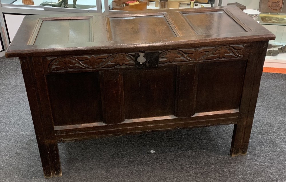 An 18th-century dark oak coffer featuring a three-panel hinged top, carved frieze rail, iron lock plate, and raised stile feet.