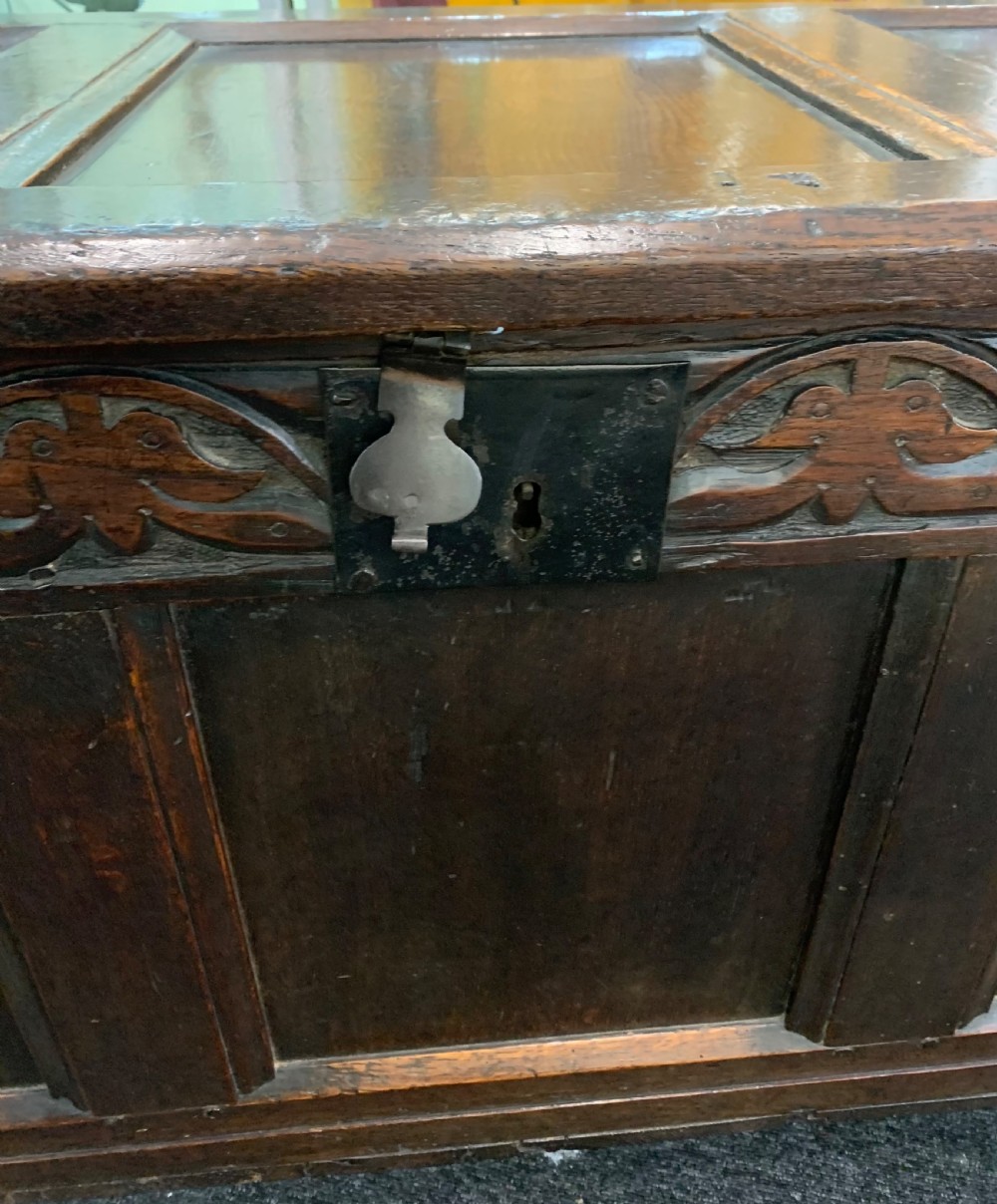 An 18th-century dark oak coffer featuring a three-panel hinged top, carved frieze rail, iron lock plate, and raised stile feet. View III