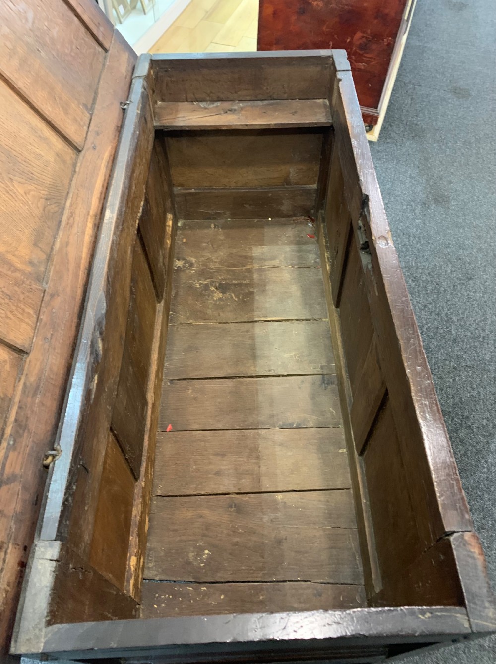 An 18th-century dark oak coffer featuring a three-panel hinged top, carved frieze rail, iron lock plate, and raised stile feet. View VI