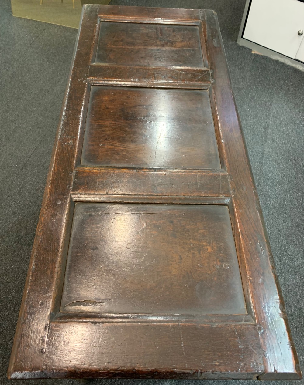 An 18th-century dark oak coffer featuring a three-panel hinged top, carved frieze rail, iron lock plate, and raised stile feet. View X