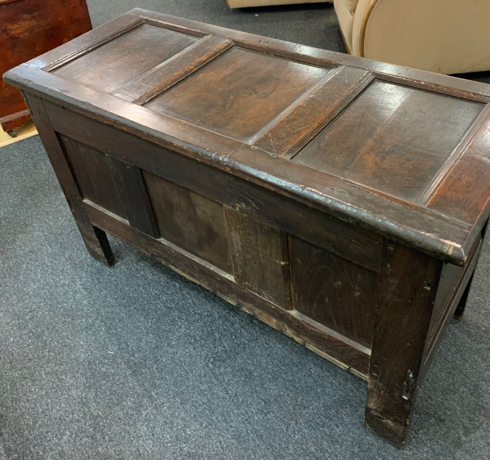 An 18th-century dark oak coffer featuring a three-panel hinged top, carved frieze rail, iron lock plate, and raised stile feet. View XII