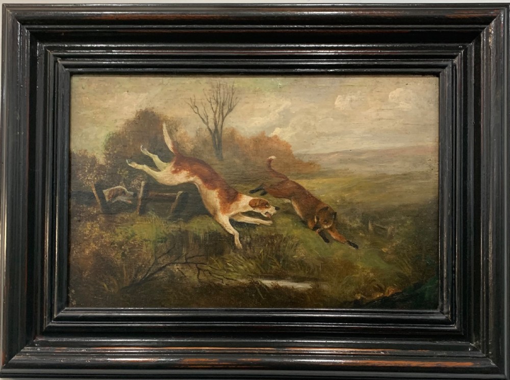 An early nineteenth-century oil painting on a wooden panel depicting two hunting hounds in pursuit of a fox across a landscape, set within a dark moulded frame.