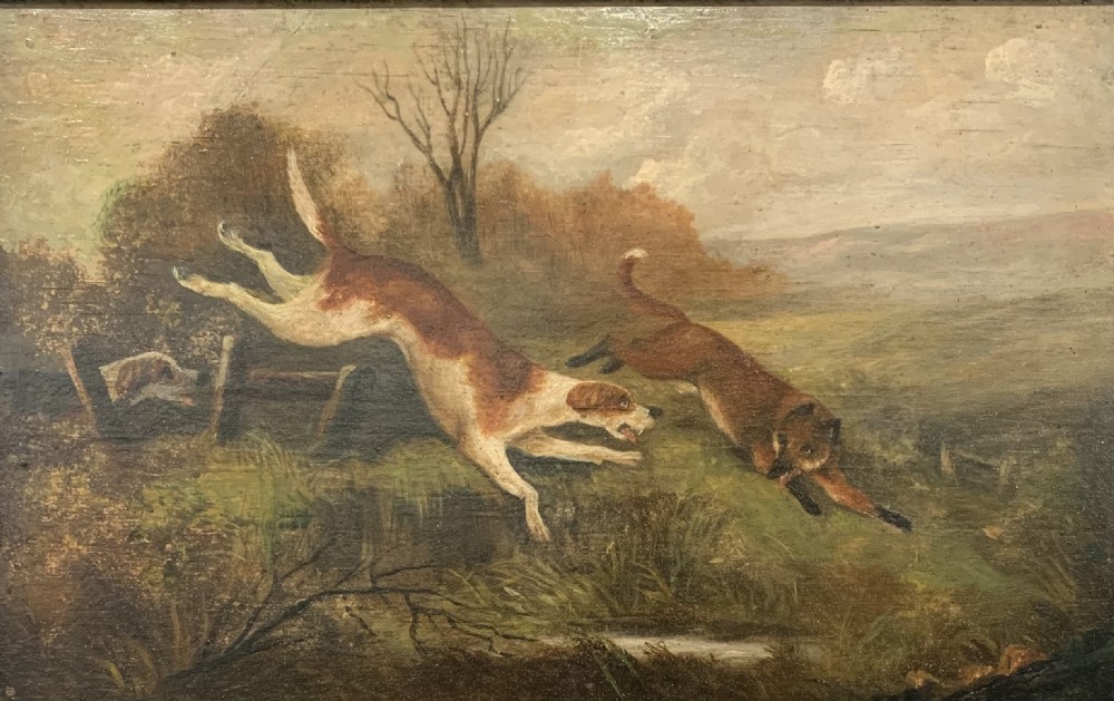 An early nineteenth-century oil painting on a wooden panel depicting two hunting hounds in pursuit of a fox across a landscape, set within a dark moulded frame. View II