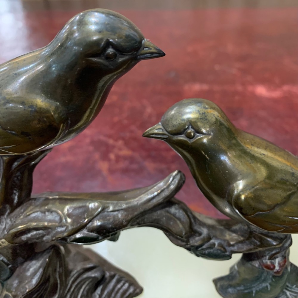 A French Art Deco mantel clock with a circular cream onyx timepiece mounted on a black marble base beside a metal bird sculpture. View IV