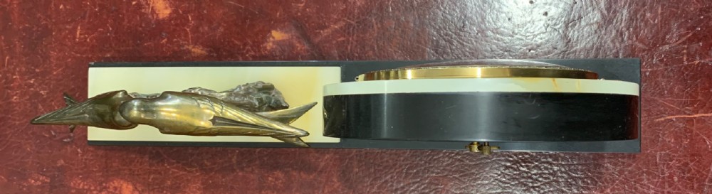 A French Art Deco mantel clock with a circular cream onyx timepiece mounted on a black marble base beside a metal bird sculpture. View V