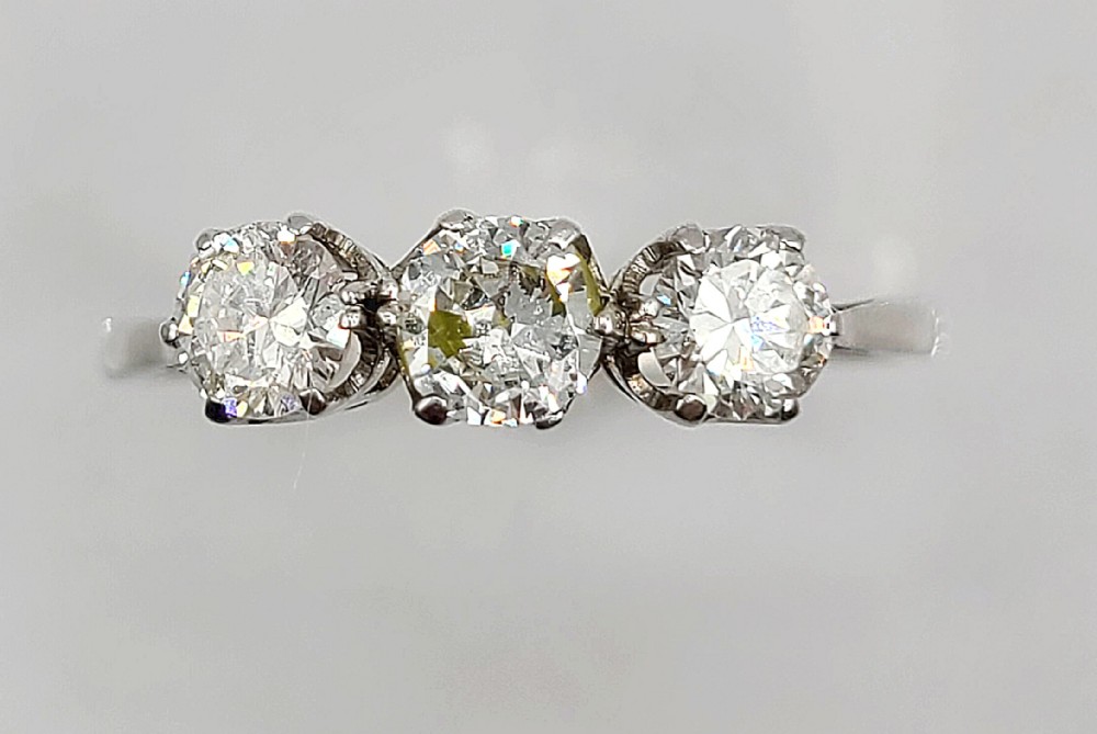 An Art Deco platinum ring featuring three round diamonds set side-by-side in claw mounts along a plain band.