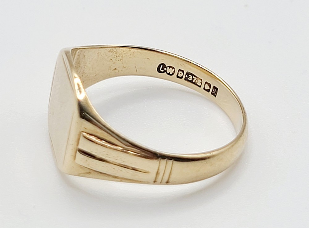 A vintage 9ct yellow gold signet ring featuring a flat cushion-shaped bezel and grooved details on the shoulders. View VI