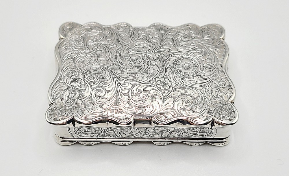 An ornate rectangular Victorian silver table snuff box featuring serpentine edges, hand-engraved scrollwork borders, and a plain polished central panel on the hinged lid. View X