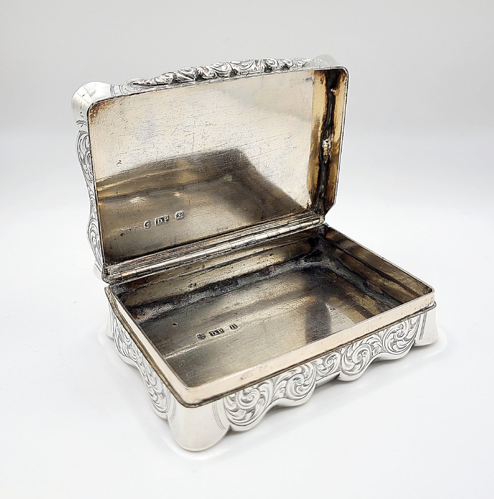 An ornate rectangular Victorian silver table snuff box featuring serpentine edges, hand-engraved scrollwork borders, and a plain polished central panel on the hinged lid. View XI