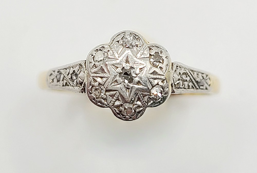 An Art Deco diamond daisy cluster ring with a platinum star-engraved setting on an 18ct yellow gold band.