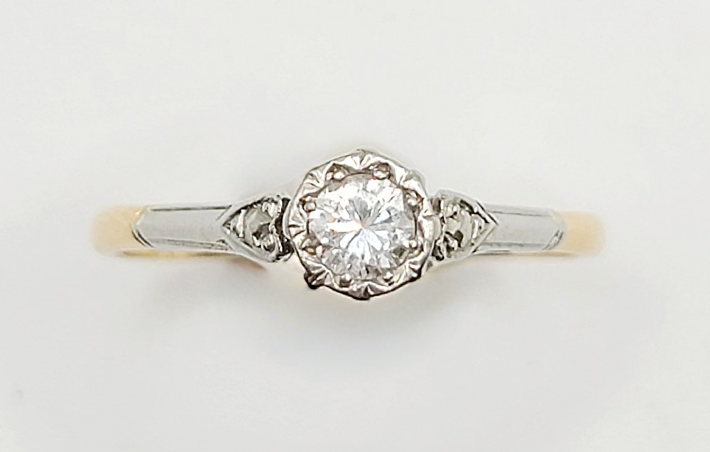 An Art Deco solitaire ring featuring a central diamond mounted in a carved platinum illusion setting on an 18ct yellow gold band.