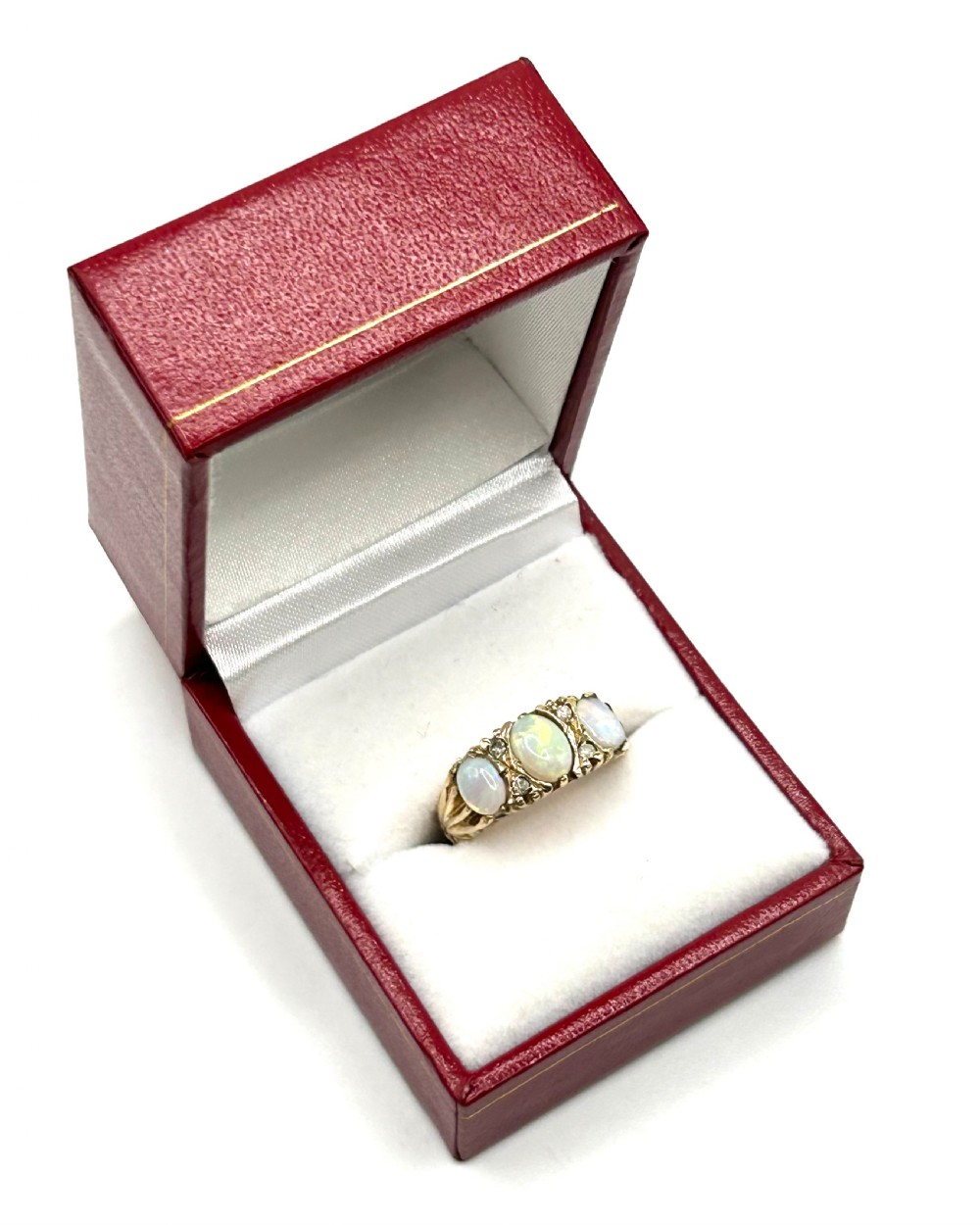 A 9ct yellow gold trilogy ring set with three oval cabochon opals and small diamond accents on carved shoulders.
