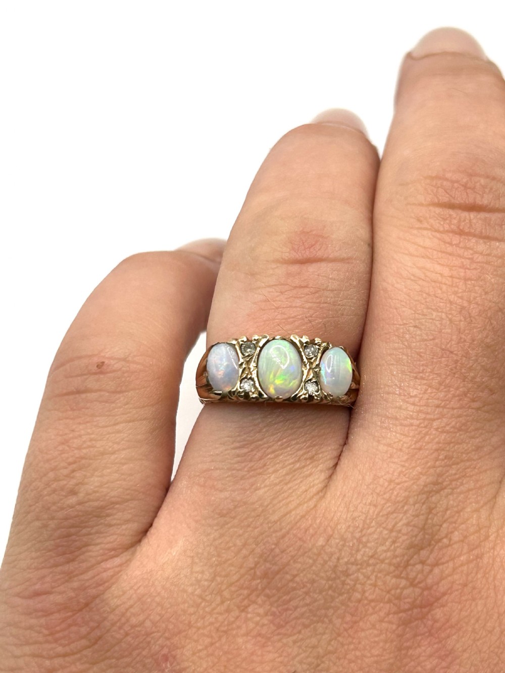 A 9ct yellow gold trilogy ring set with three oval cabochon opals and small diamond accents on carved shoulders. View II
