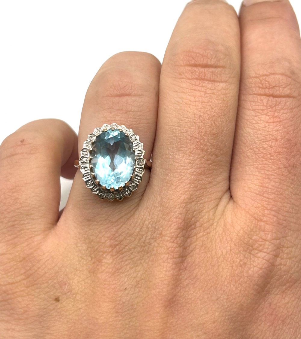 A vintage 9ct gold ring featuring a large oval light blue topaz surrounded by a halo of small diamonds. View II