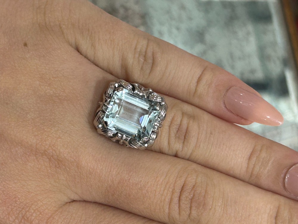 An emerald-cut light blue aquamarine gemstone set in a white gold claw mount inside a black presentation box. View V