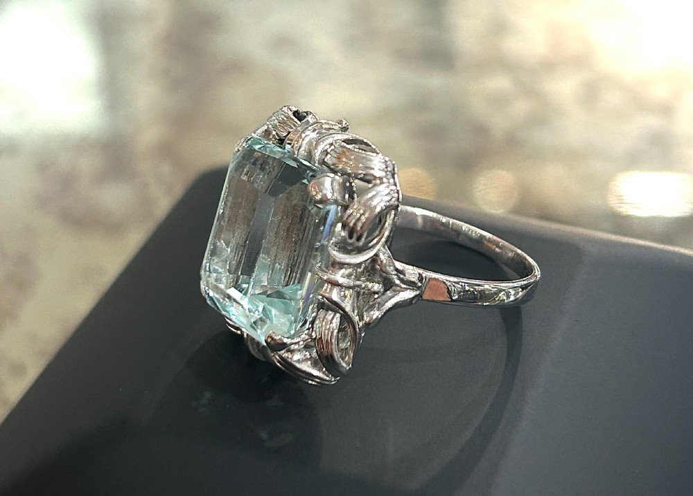 An emerald-cut light blue aquamarine gemstone set in a white gold claw mount inside a black presentation box. View II