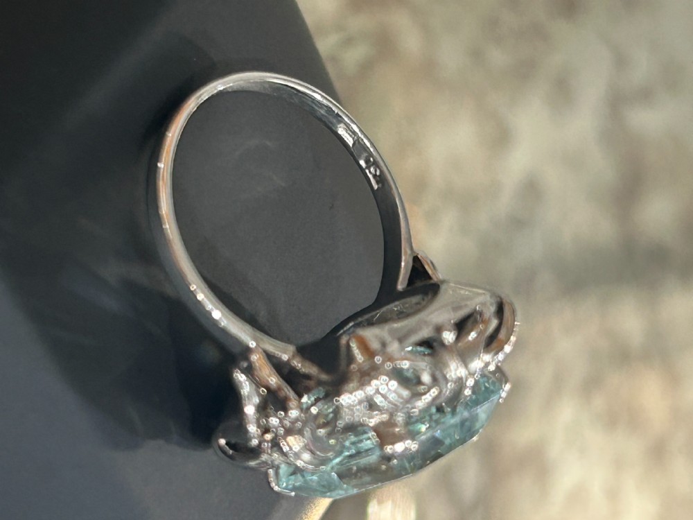 An emerald-cut light blue aquamarine gemstone set in a white gold claw mount inside a black presentation box. View III