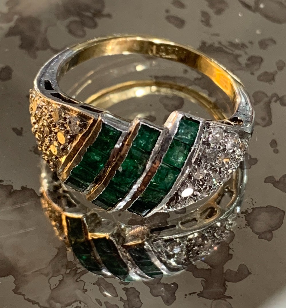 An Art Deco 18ct yellow and white gold cluster ring featuring diagonal rows of square green emeralds flanked by pave-set diamonds.