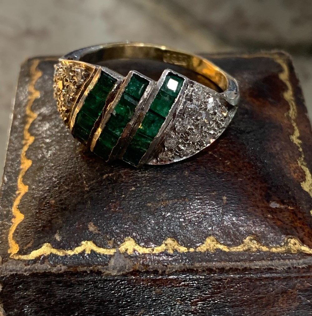An Art Deco 18ct yellow and white gold cluster ring featuring diagonal rows of square green emeralds flanked by pave-set diamonds. View II
