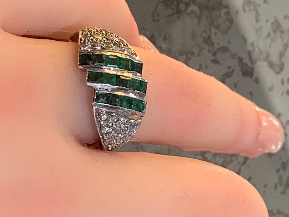 An Art Deco 18ct yellow and white gold cluster ring featuring diagonal rows of square green emeralds flanked by pave-set diamonds. View IV