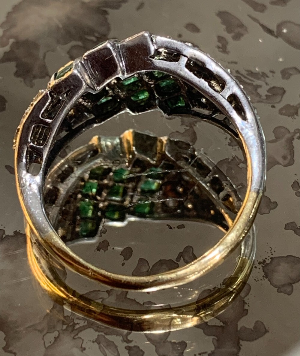 An Art Deco 18ct yellow and white gold cluster ring featuring diagonal rows of square green emeralds flanked by pave-set diamonds. View VI