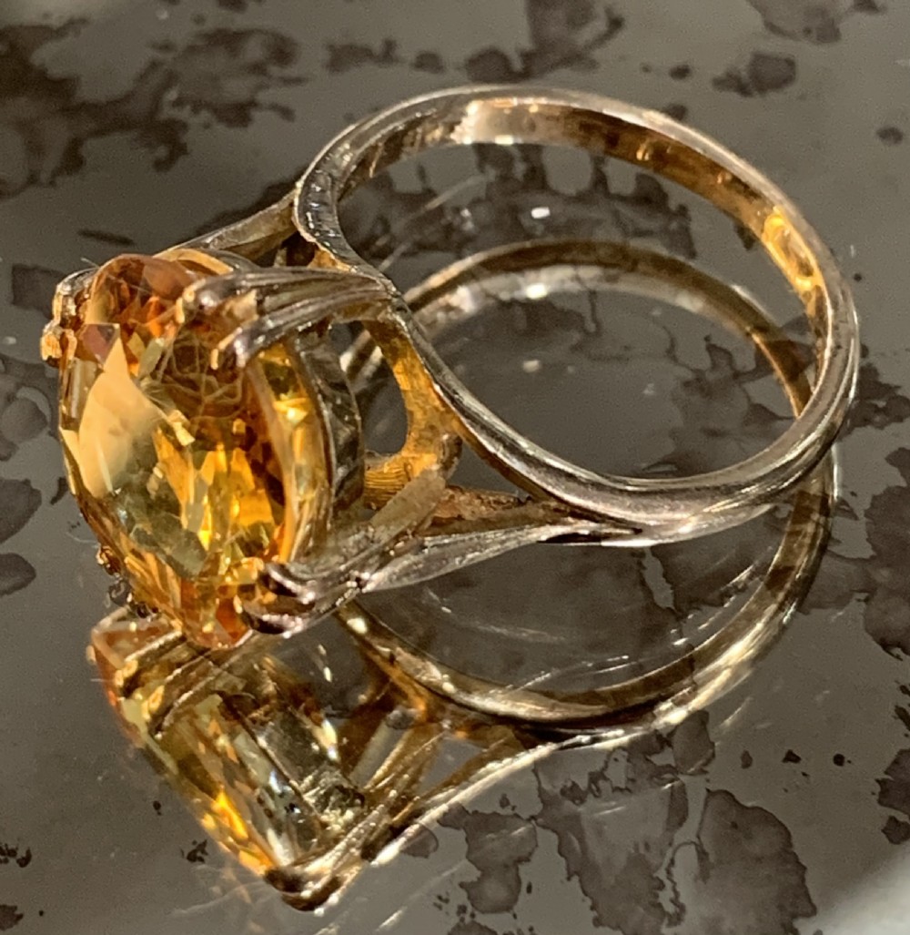 An Art Deco period 9ct gold solitaire ring featuring a large faceted orange synthetic sapphire held in claw settings. View II