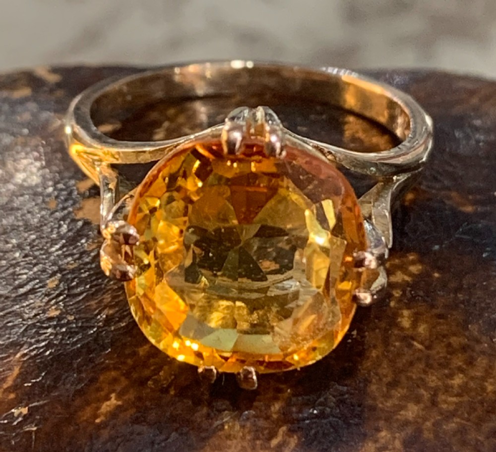An Art Deco period 9ct gold solitaire ring featuring a large faceted orange synthetic sapphire held in claw settings.