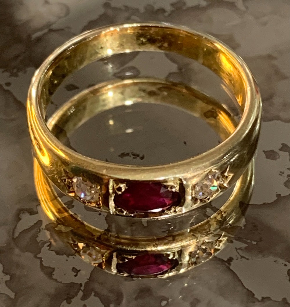 An 18ct yellow gold Victorian gypsy ring featuring a central oval red ruby flanked by two star-set diamonds set flush into the wide band.