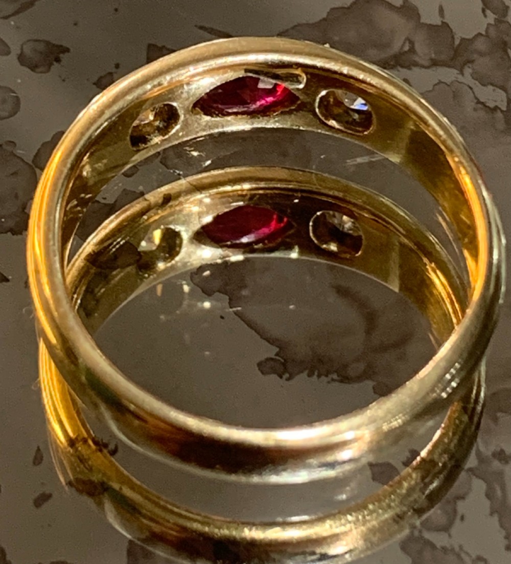 An 18ct yellow gold Victorian gypsy ring featuring a central oval red ruby flanked by two star-set diamonds set flush into the wide band. View II