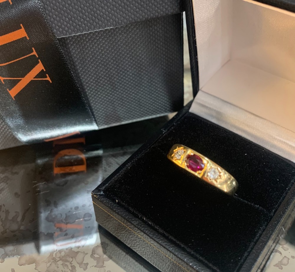 An 18ct yellow gold Victorian gypsy ring featuring a central oval red ruby flanked by two star-set diamonds set flush into the wide band. View V