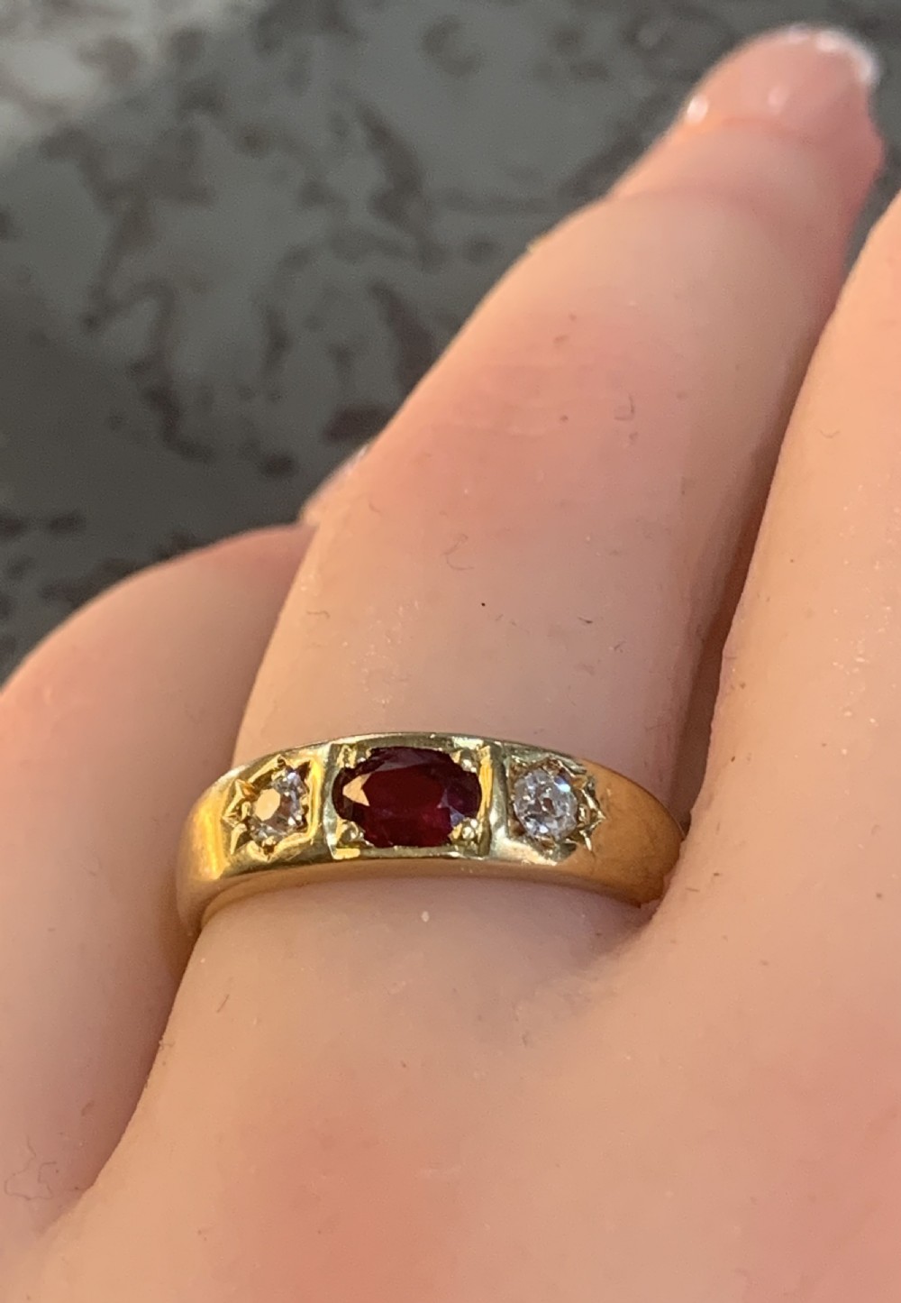 An 18ct yellow gold Victorian gypsy ring featuring a central oval red ruby flanked by two star-set diamonds set flush into the wide band. View VI