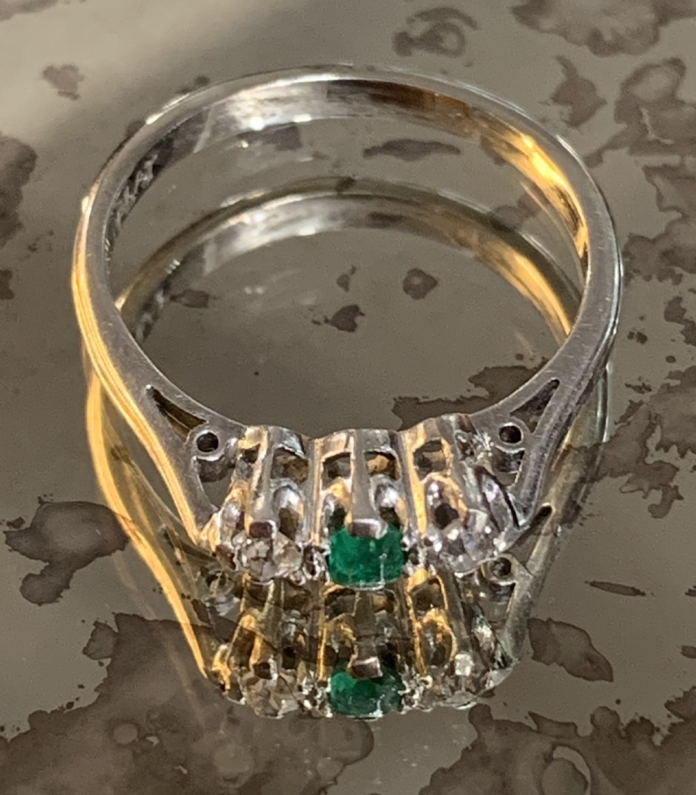 An Edwardian platinum trilogy ring featuring a central round green emerald flanked by two old cut diamonds in a claw setting.