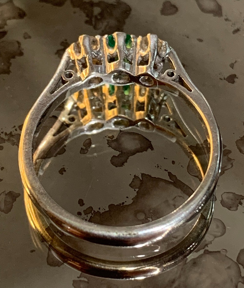 An Edwardian platinum trilogy ring featuring a central round green emerald flanked by two old cut diamonds in a claw setting. View III
