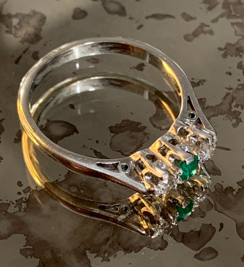 An Edwardian platinum trilogy ring featuring a central round green emerald flanked by two old cut diamonds in a claw setting. View VIII