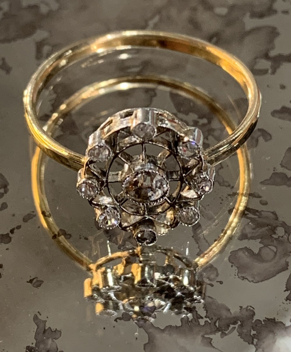 An Art Deco cluster ring featuring a central round diamond surrounded by a circular halo of smaller diamonds set in platinum with a yellow gold band.