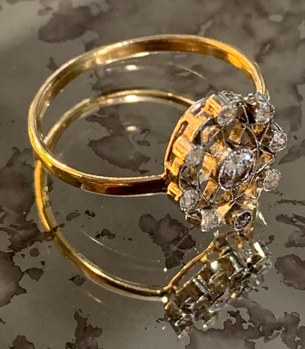 An Art Deco cluster ring featuring a central round diamond surrounded by a circular halo of smaller diamonds set in platinum with a yellow gold band. View II