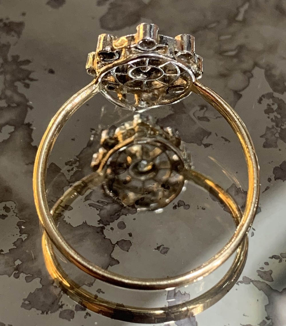 An Art Deco cluster ring featuring a central round diamond surrounded by a circular halo of smaller diamonds set in platinum with a yellow gold band. View III