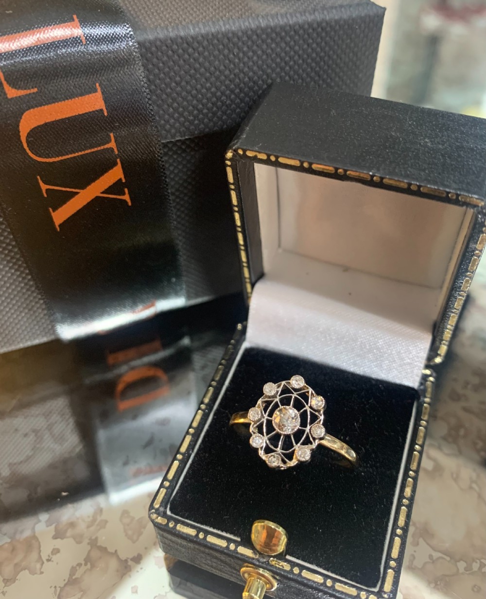 An Art Deco cluster ring featuring a central round diamond surrounded by a circular halo of smaller diamonds set in platinum with a yellow gold band. View IV