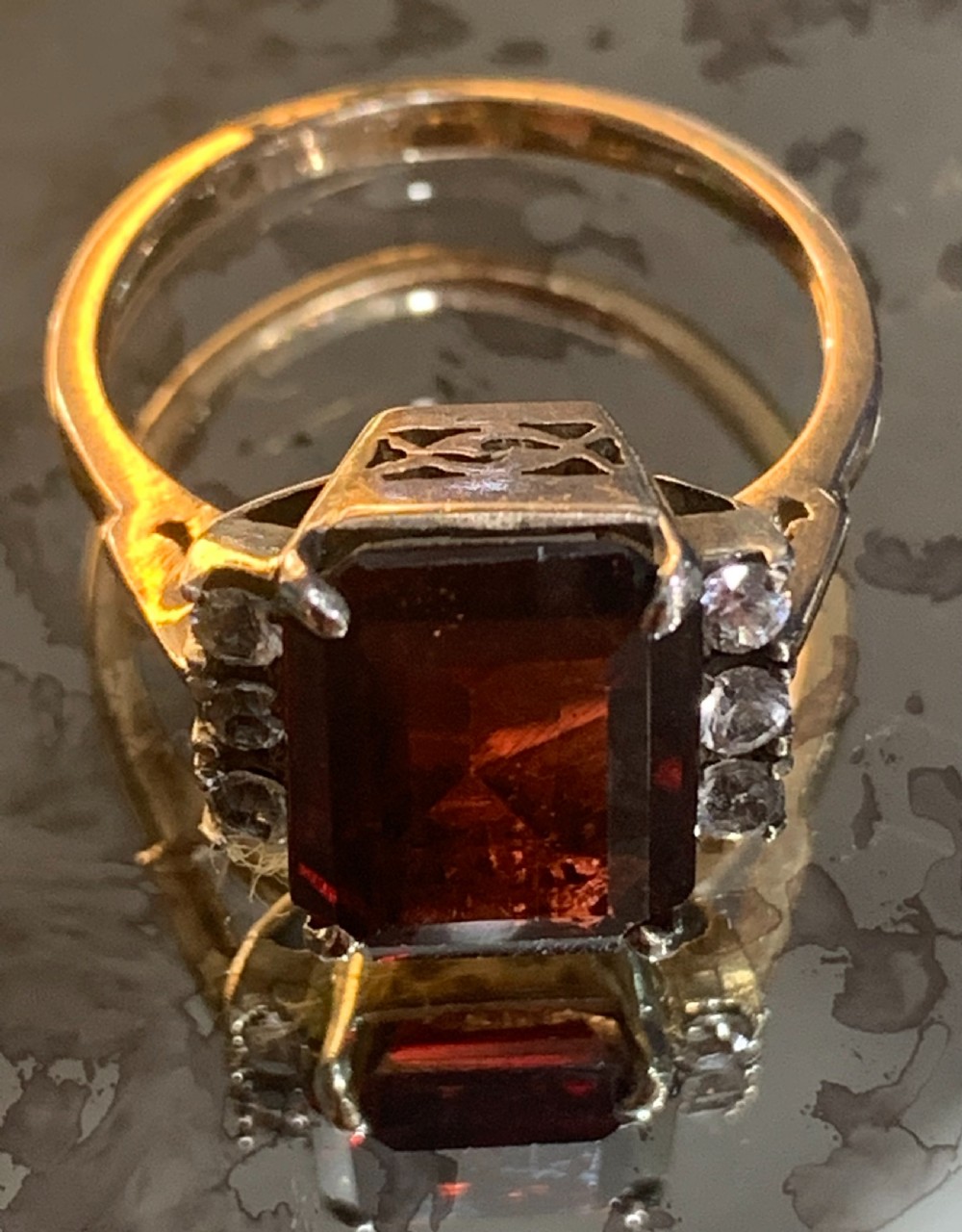 An emerald-cut red garnet set in 9ct gold with white sapphire side stones and geometric gallery work.