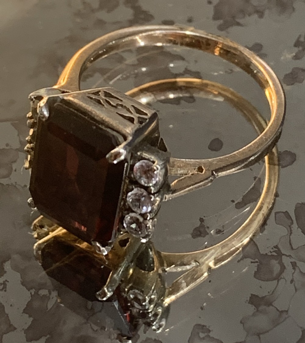 An emerald-cut red garnet set in 9ct gold with white sapphire side stones and geometric gallery work. View III