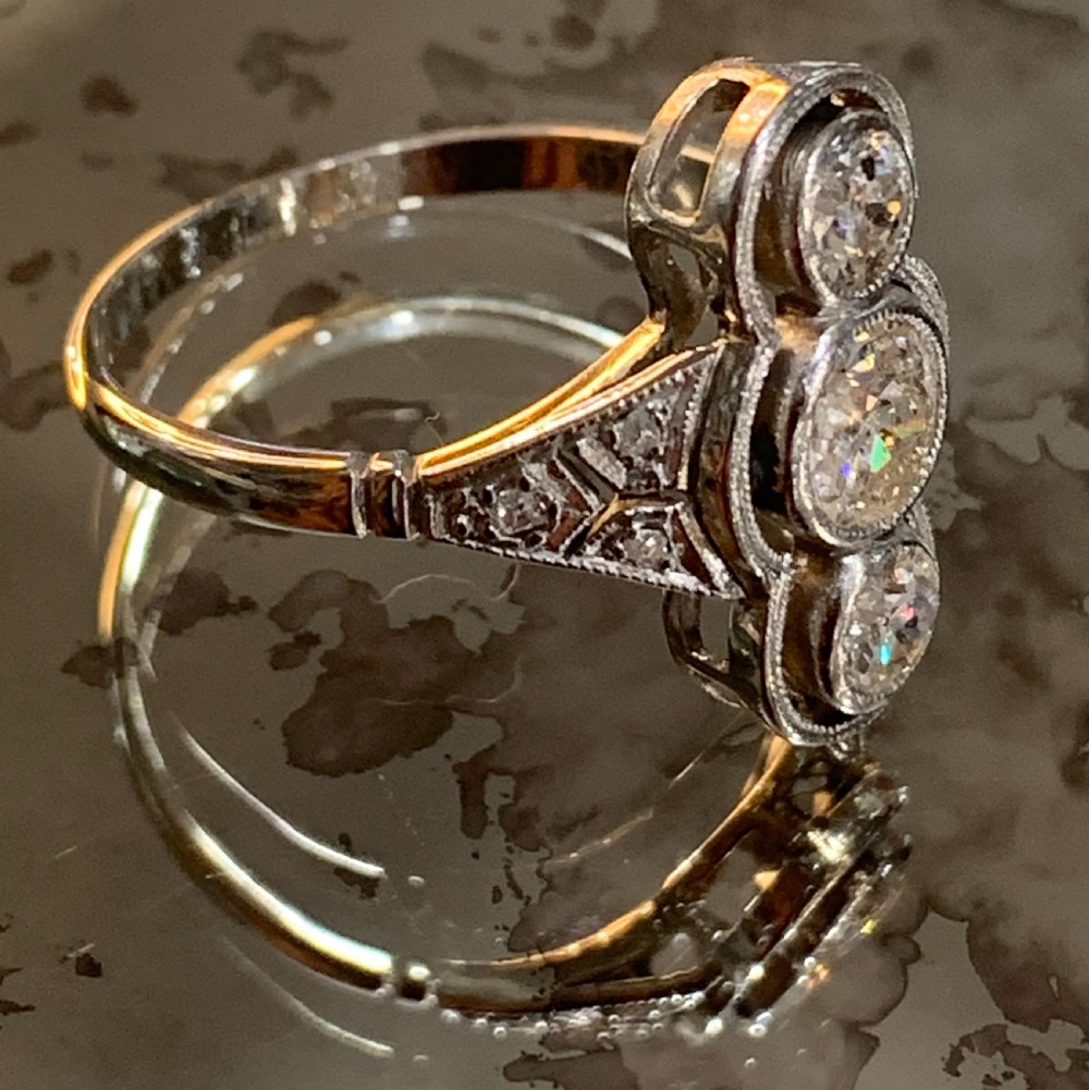 An antique Art Deco platinum ring featuring three vertically aligned old-cut diamonds with intricate millegrain detailing. View VI