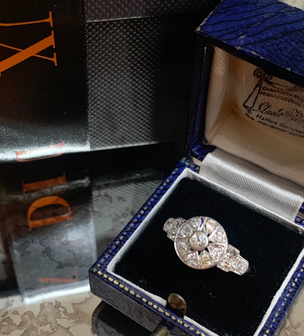 An Art Deco platinum cluster ring featuring a central round diamond framed by smaller diamonds in a geometric starburst setting with stepped shoulders. View II